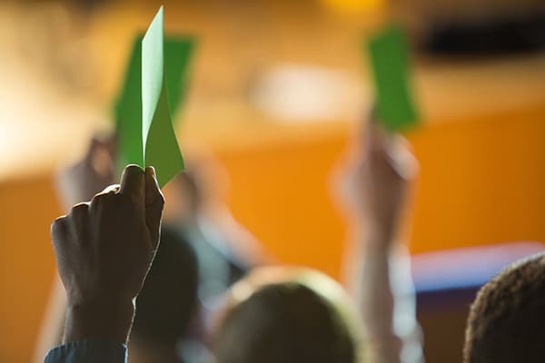 A hand raises a ballot in the air during a members meeting